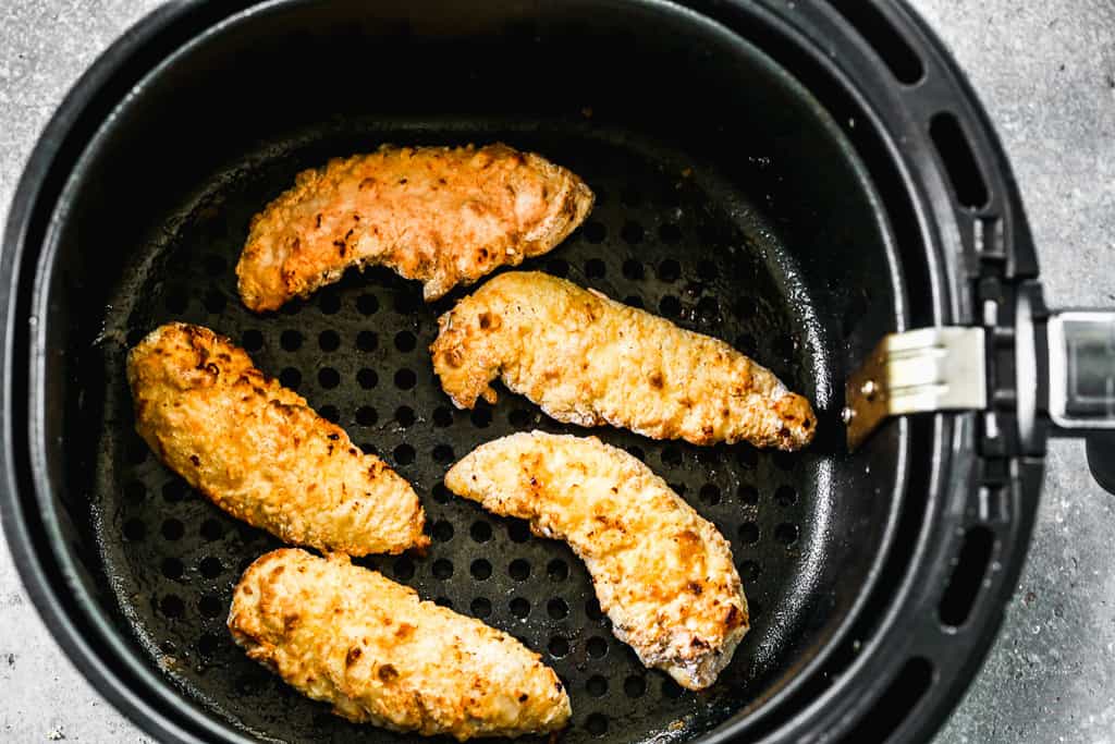 Chicken tenders cooking in an air fryer basket.