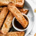 A plate with Air Fryer French Toast and a small container of syrup.