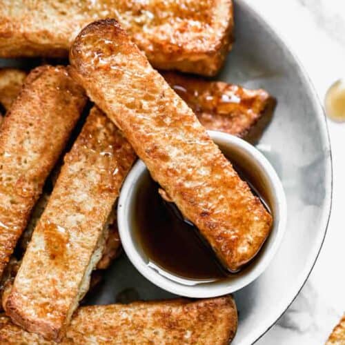 A plate with Air Fryer French Toast and a small container of syrup.