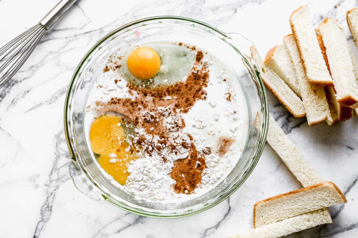 All of the ingredients for french toast in a shallow dish, with pieces of bread cut into thirds for easy french toast sticks.