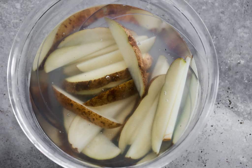 Potato wedges soaking in a bowl of water.