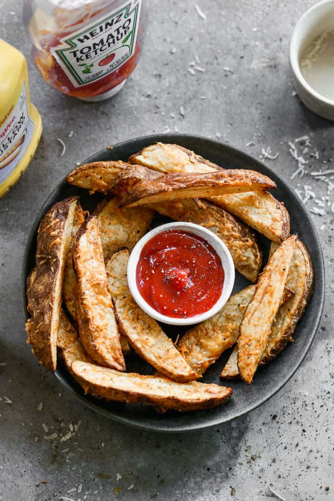 Crispy potatoes wedges served on a plate, with ketchup for dipping.