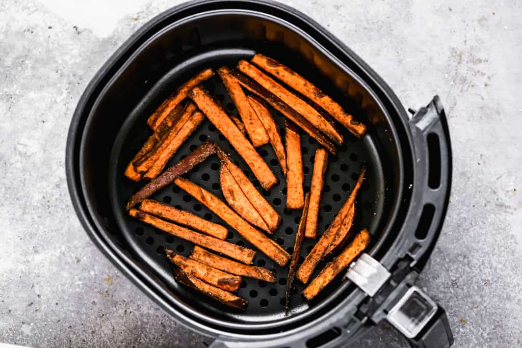 Cooked sweet potato fries in the basket of an air fryer.