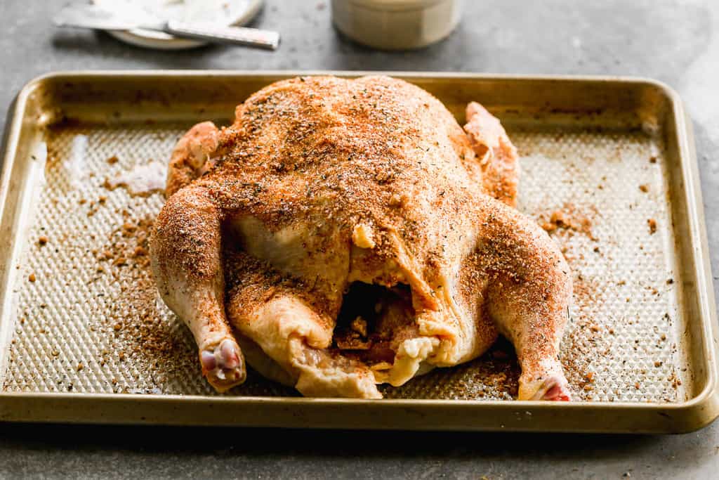 A whole chicken with poultry seasoning all over it, ready to cook in the air fryer.