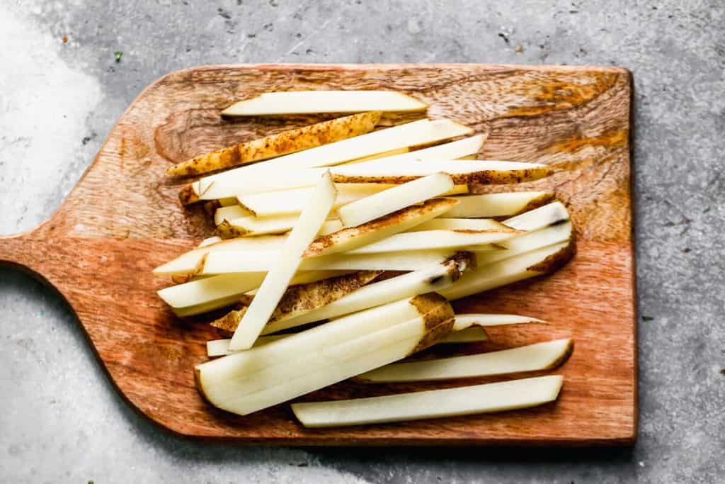 Russet potatoes on a cutting board, cut into matchsticks to make French fries.