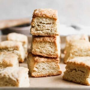 Three baked angel biscuits stacked on top of each other, on a baking sheet with more biscuits.