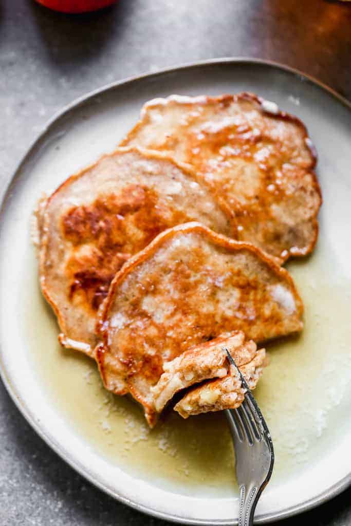 Three apple pancakes on a plate with a fork taking a bite.