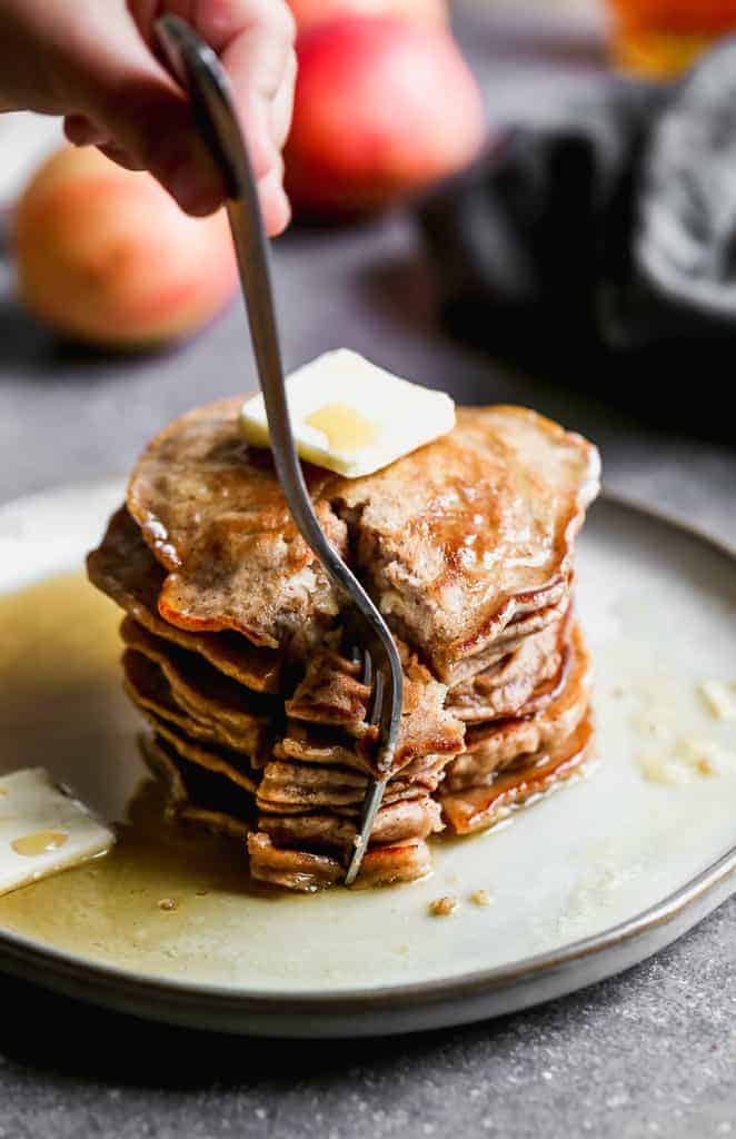 A large stack of pancakes with a wedge cut out and a fork piercing them.