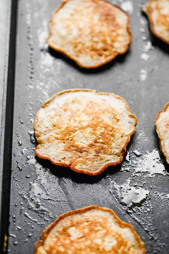 Apple pancakes cooking on a hot griddle.