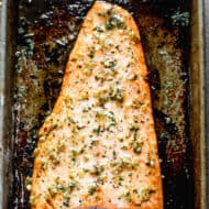 Baked salmon fillet on a sheet pan with lemon garlic butter sauce topping.