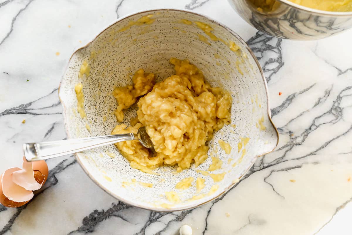 Three bananas in a ceramic bowl, mashed with a fork.