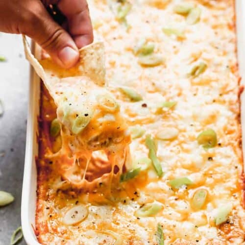 A pan of bean dip with a hand dipping a tortilla chip in it.