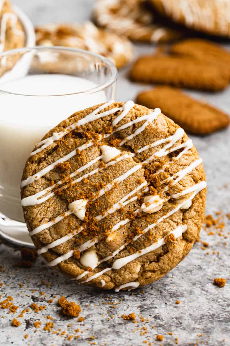 A homemade lotus biscoff cookie leaning against a small glass of milk.