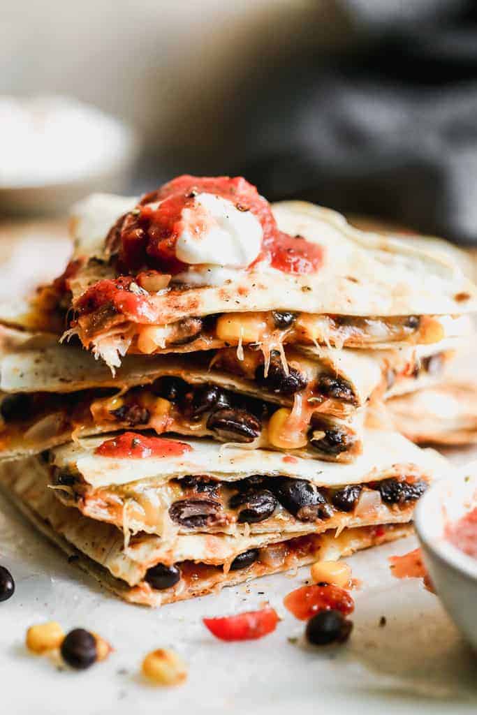 A stack of cut black bean quesadillas with salsa and sour cream on top.