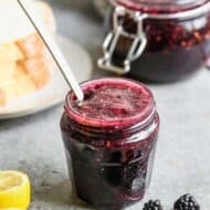 A jar of homemade Blackberry jam, with a small spoon resting inside.