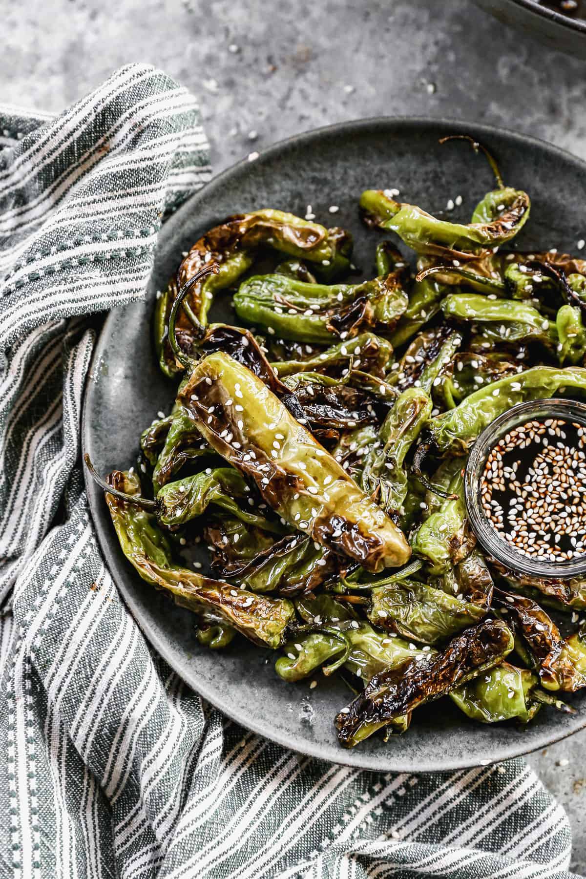 A close-up image of Blistered Shishito Peppers drizzled with honey and soy sauce, and sprinkled with sesame seeds.