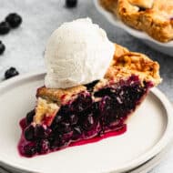 A slice of homemade Blueberry Pie on a plate, topped with vanilla bean ice cream.