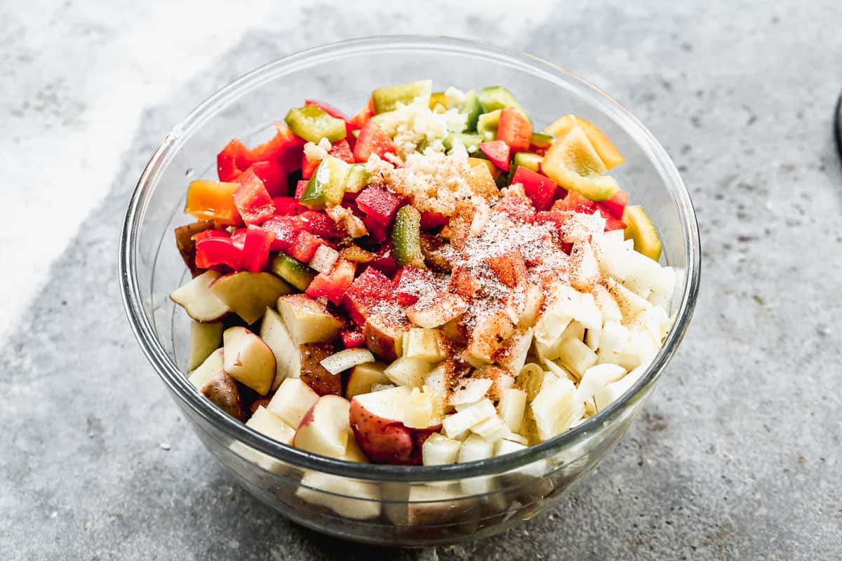 Red potatoes, garlic, onion, bell peppers, olive oil, butter, seasoned salt, cayenne pepper, salt, and pepper in a large bowl to make homemade breakfast potatoes.