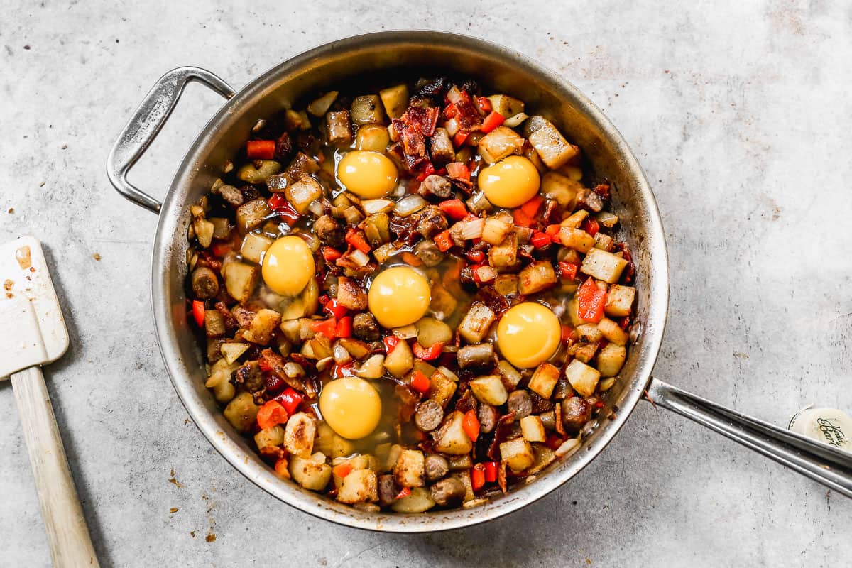 The best Breakfast Skillet with five freshly cracked eggs cooking on top, in a stainless steel pan.