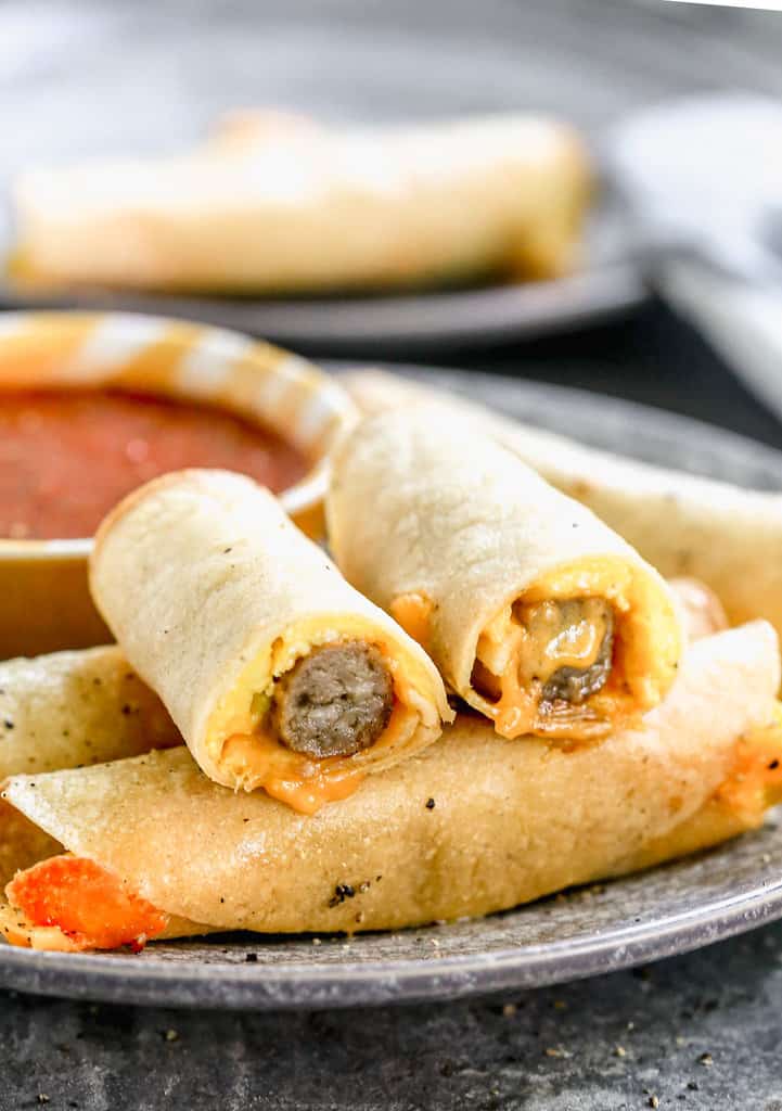 A plate of breakfast taquitos with one of them cut in half.