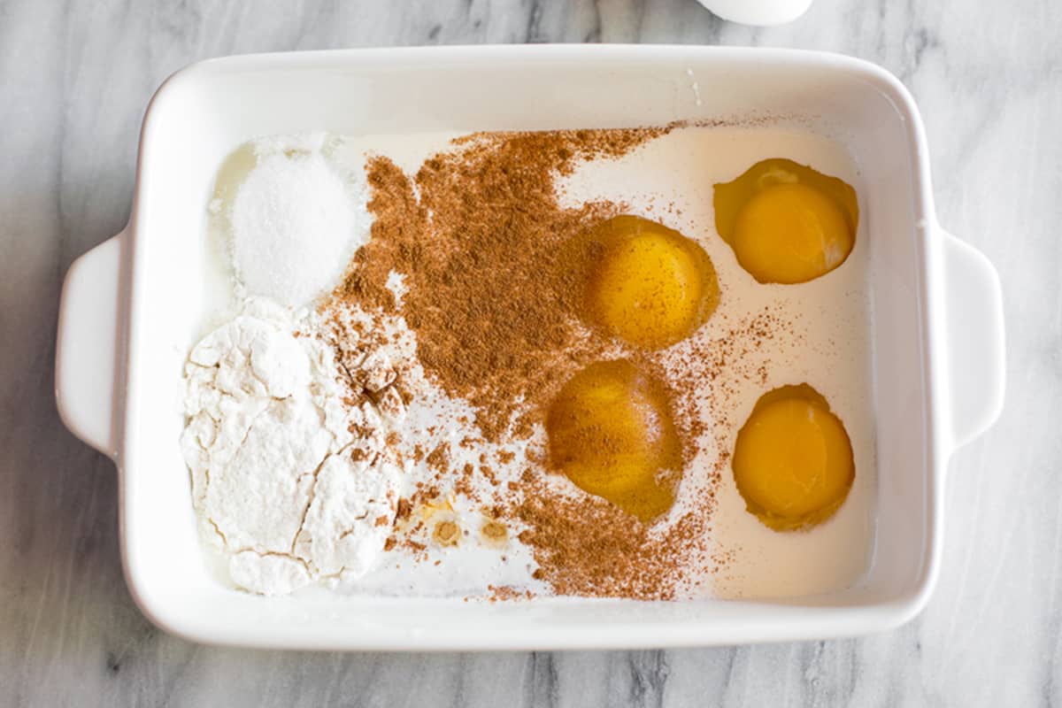 A white dish filled with eggs, cream, cinnamon, sugar, and flour to make easy brioche french toast.