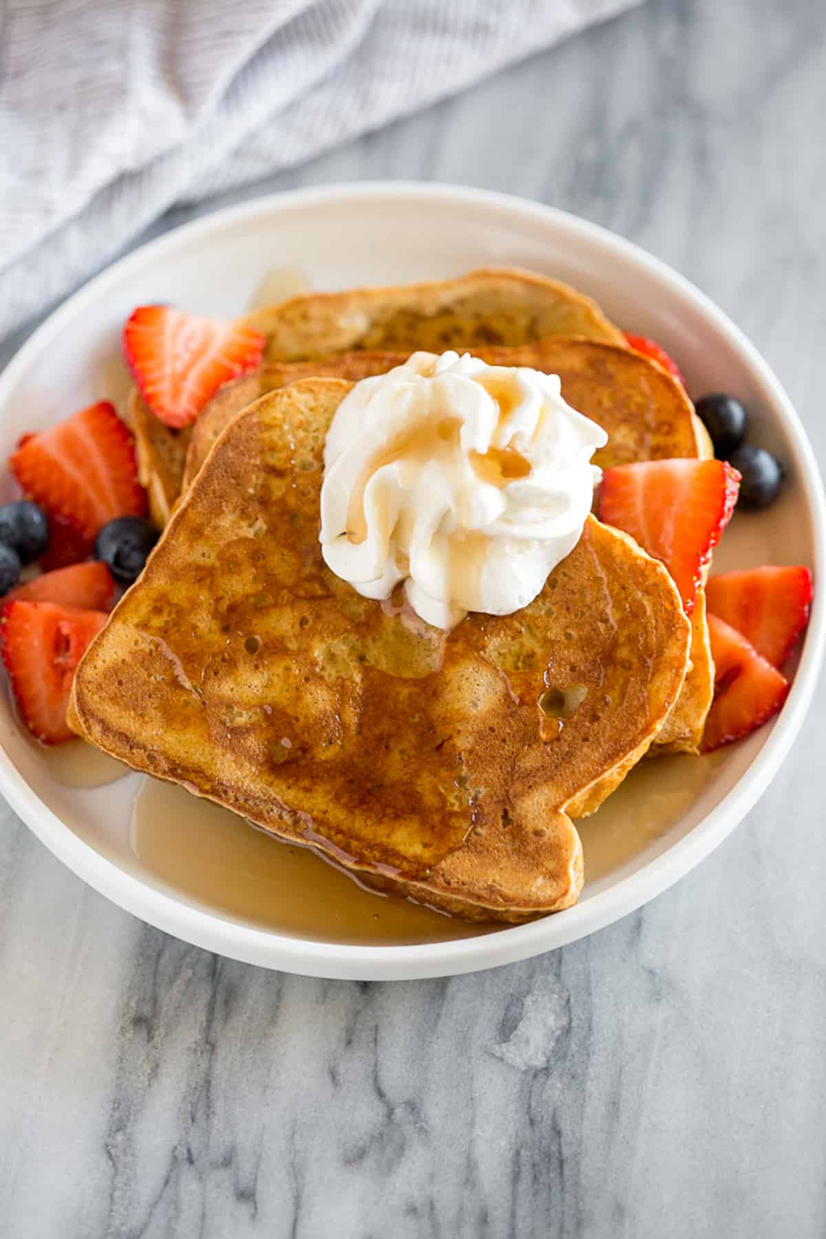 The best Brioche French Toast recipe, stacked and topped with whipped cream and a side of berries.