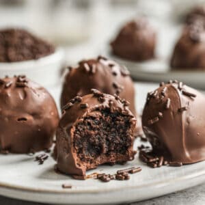 Four homemade brownie truffles on a plate, the one in the front is bitten in half.