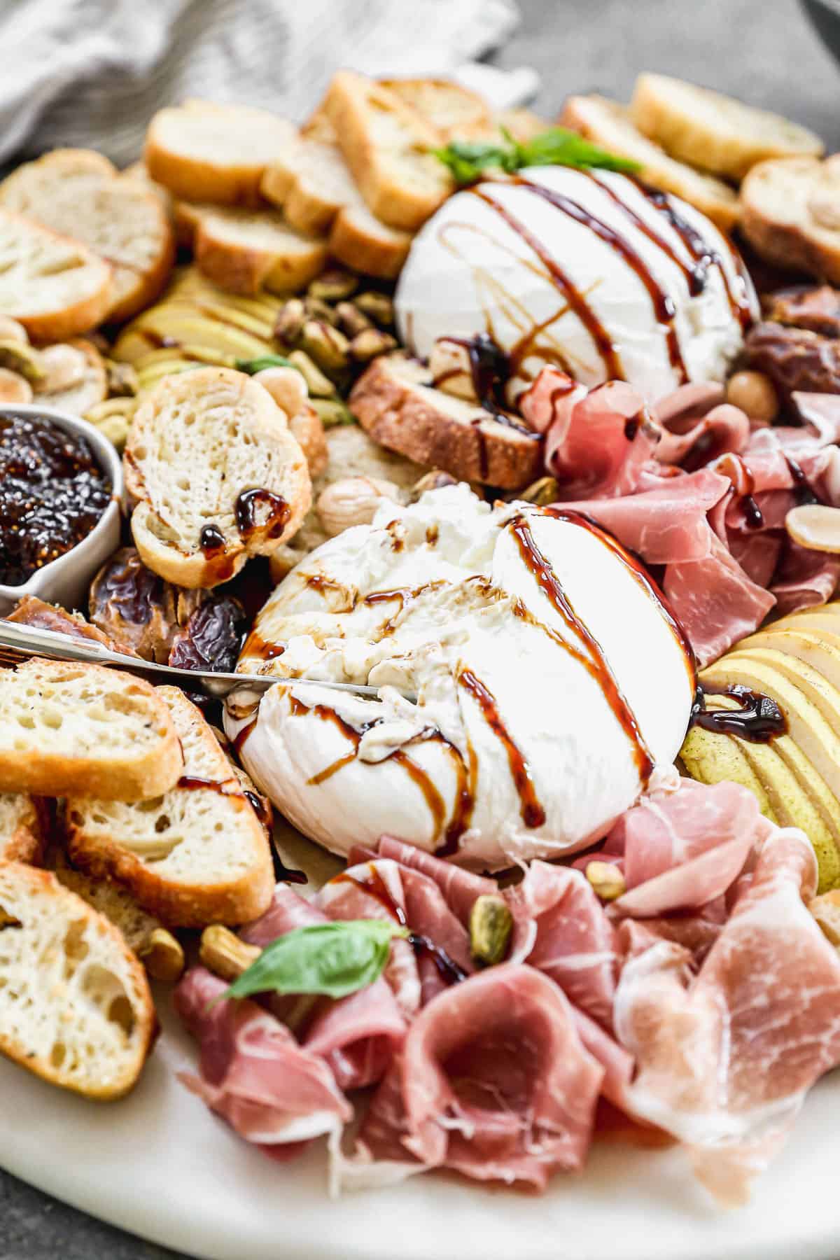 A close up image of the burrata drizzled with balsamic reduction and being sliced into from the burrata appetizer