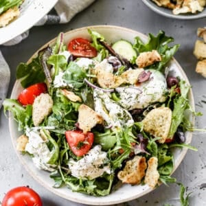 Burrata salad served in a bowl, with fresh herbs and pita chips on top.