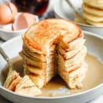 A stack of buttermilk pancakes with a big bite taken out by a fork.