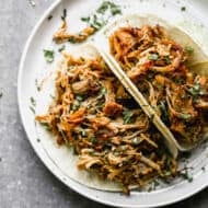 Two of the best carnitas recipe on a plate, topped with fresh cilantro.