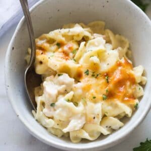 A ceramic bowl filled with chicken noodle casserole with a silver spoon in it and another bowl in the background.