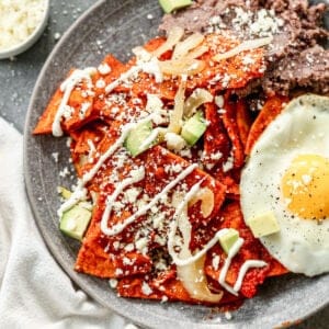 Chilaquiles served on a plate, garnished with cream, cotija and a side of beans and fried egg.