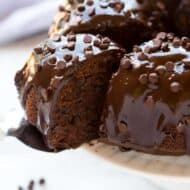 A slice of chocolate bundt cake being served from a cake stand with the whole cake on it.