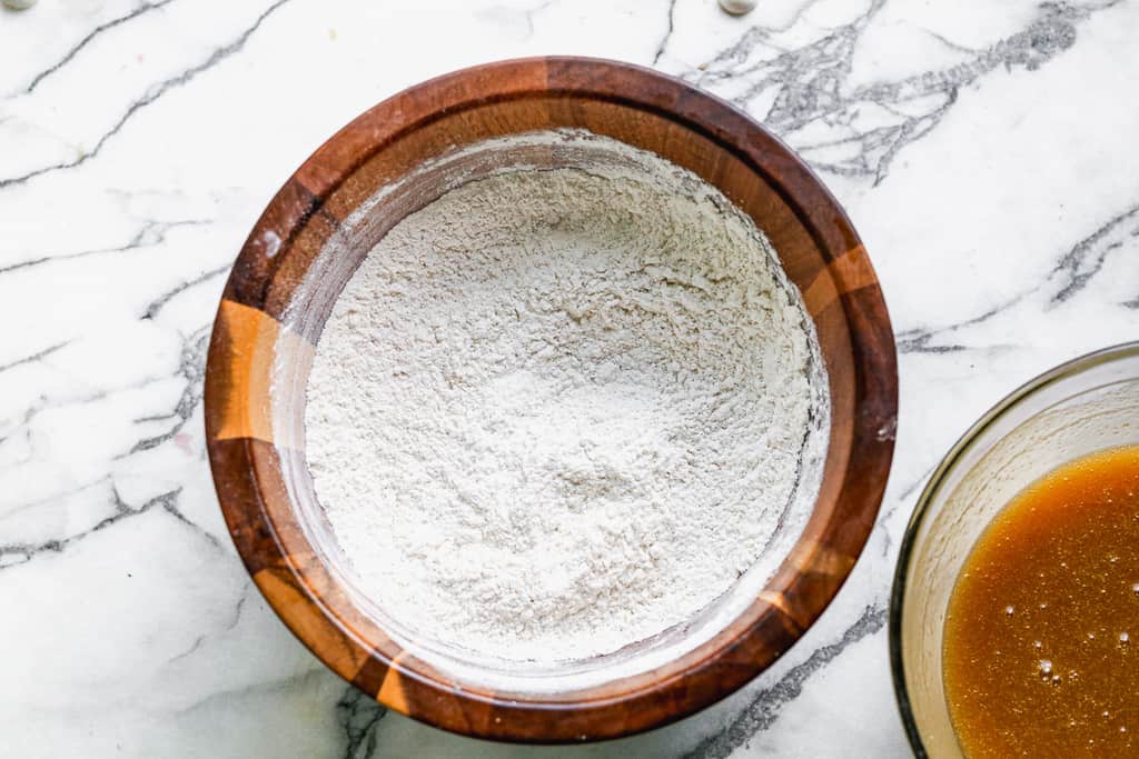 A wooden mixing bowl with flour, baking soda and salt.