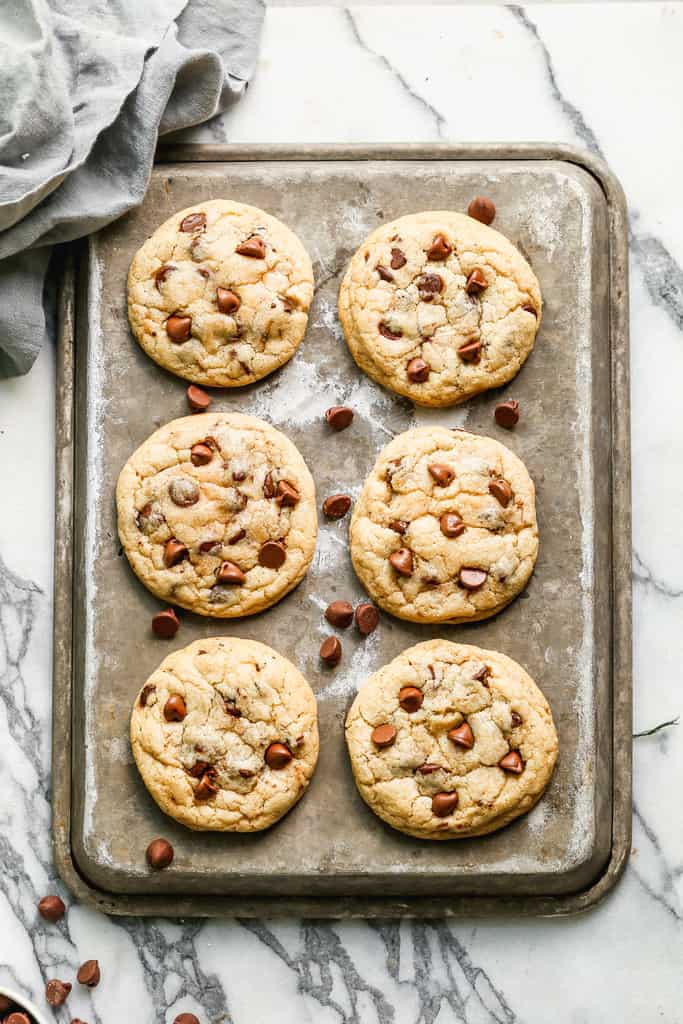 Six baked chocolate chip cookies on a baking sheet.