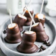 A plate of chocolate covered marshmallows that have been double stacked on a candy stick.