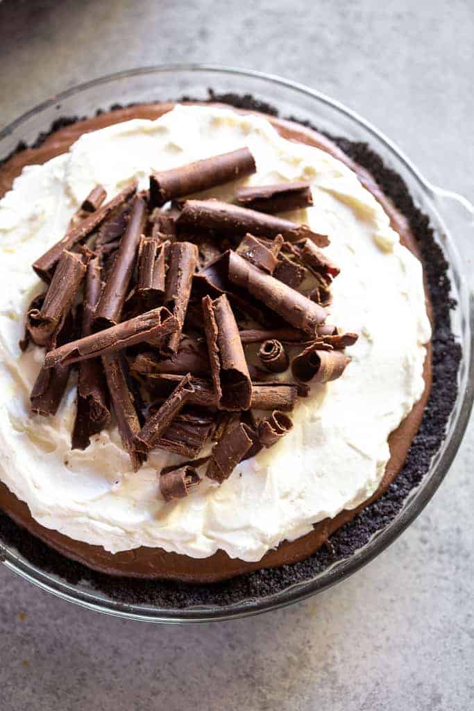 Chocolate cream pie with an oreo crust, baked in a clear pie dish, with whipped cream and chocolate curls on top.