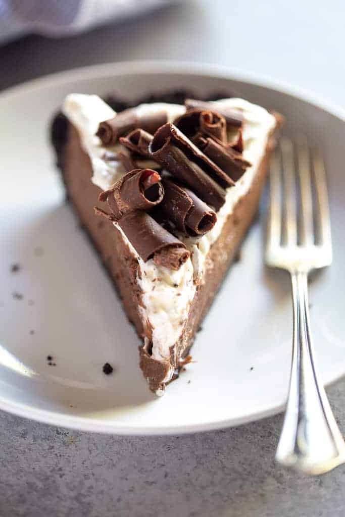 A front view of a slice of chocolate cream pie with whipped cream and chocolate curls on top. 