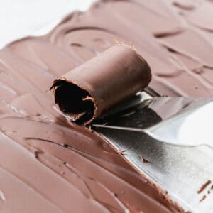 A close-up image of a spatula scraping a chocolate curl on the back of a baking sheet.