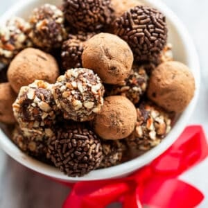 A variety of chocolate truffles homemade and in a white bowl with a red bow tied around it.