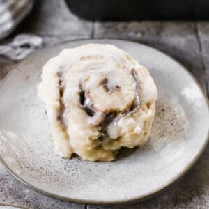 A homemade Cinnamon Roll Biscuit on a white plate, covered in cream cheese frosting.