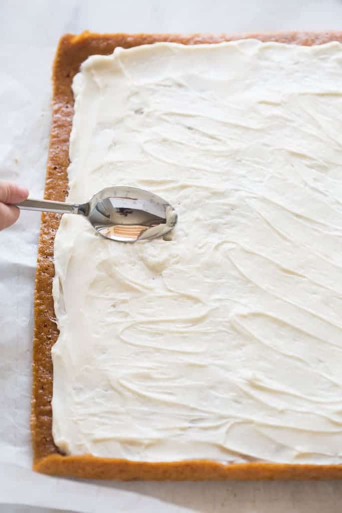 The cooked and cooled pumpkin roll laying on parchment paper with cream cheese filling being spread evenly on top.