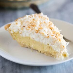 A slice of coconut cream pie on a white plate with a fork.