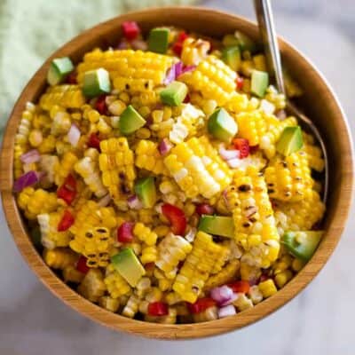 Corn salad made with grilled sweet corn, diced avocado, bell pepper and onion served in a wooden bowl with a spoon.