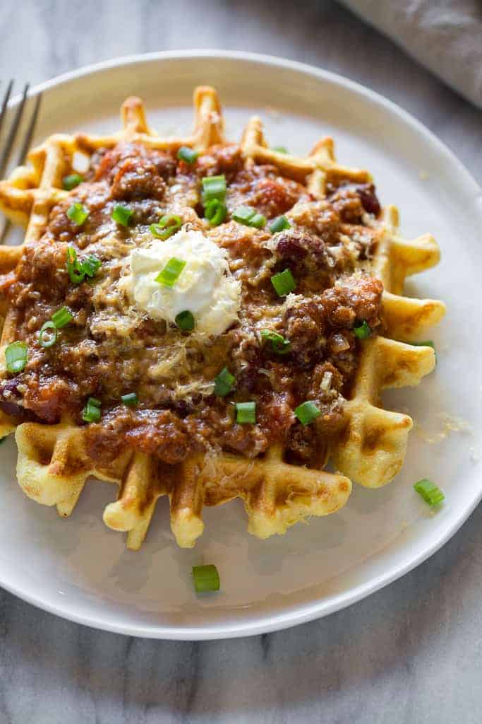 Close up photo of a waffles with chili, sour cream and chopped green onions on it.