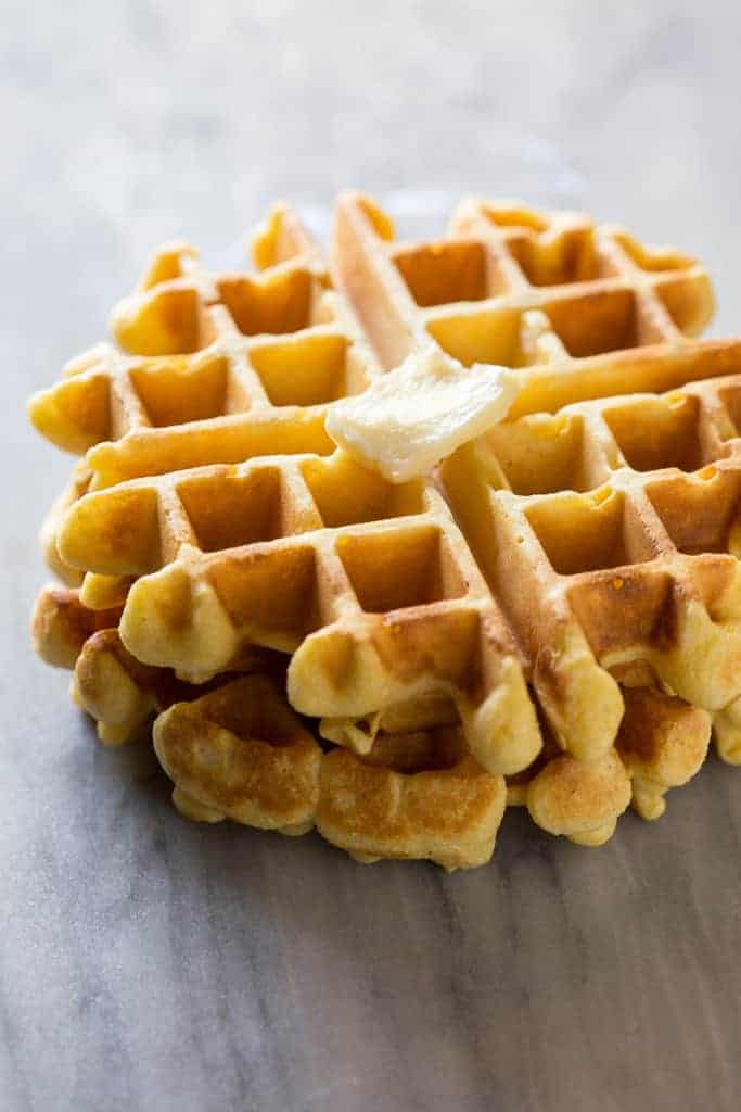 Two cornbread waffles stacked on each other on a white marble board with a piece of butter on top.