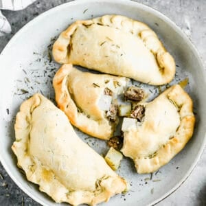 A plate with the Best Cornish Pasties made with beef and potatoes, with one of them broken in half.