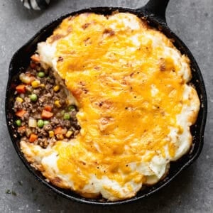 An easy Cottage Pie recipe in a cast iron pan with some meat and vegetable gravy showing under the layer of cheesy mashed potatoes.