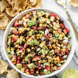 Cowboy Caviar in a white serving bowl with chips, sliced limes, and a spoon around it.